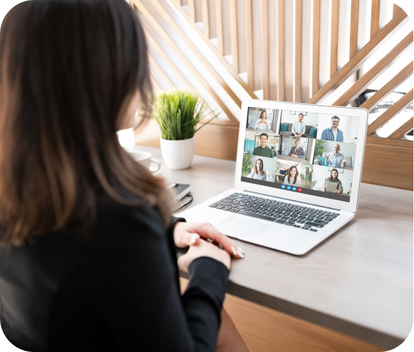 Looking over the shoulder of a woman who is looking at a laptop screen that has a virtual call with multiple people